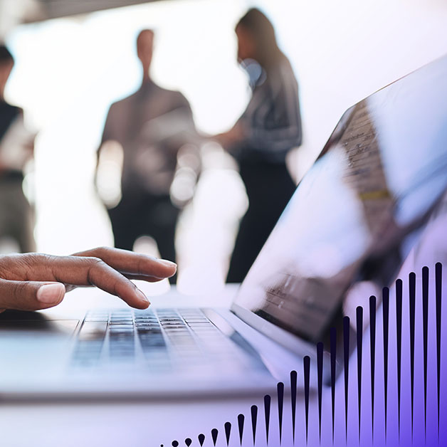 Person typing on laptop with three people standing and talking in the background