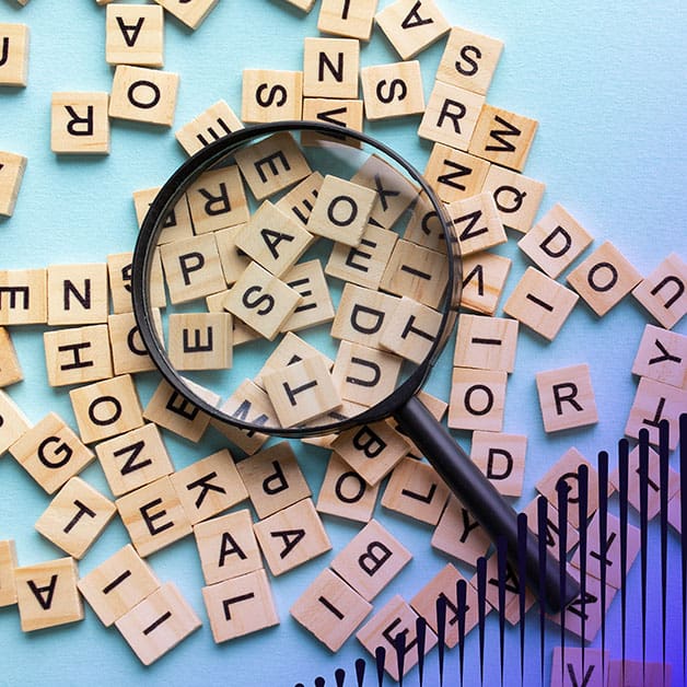 Scrabble tiles scattered across a blue surface with a magnifying glass resting on top