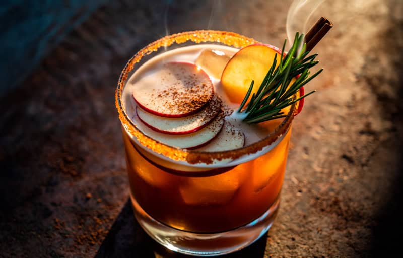 Apple cider margarita with sugar rim, apple slices, rosemary sprig, and smoking cinnamon stick